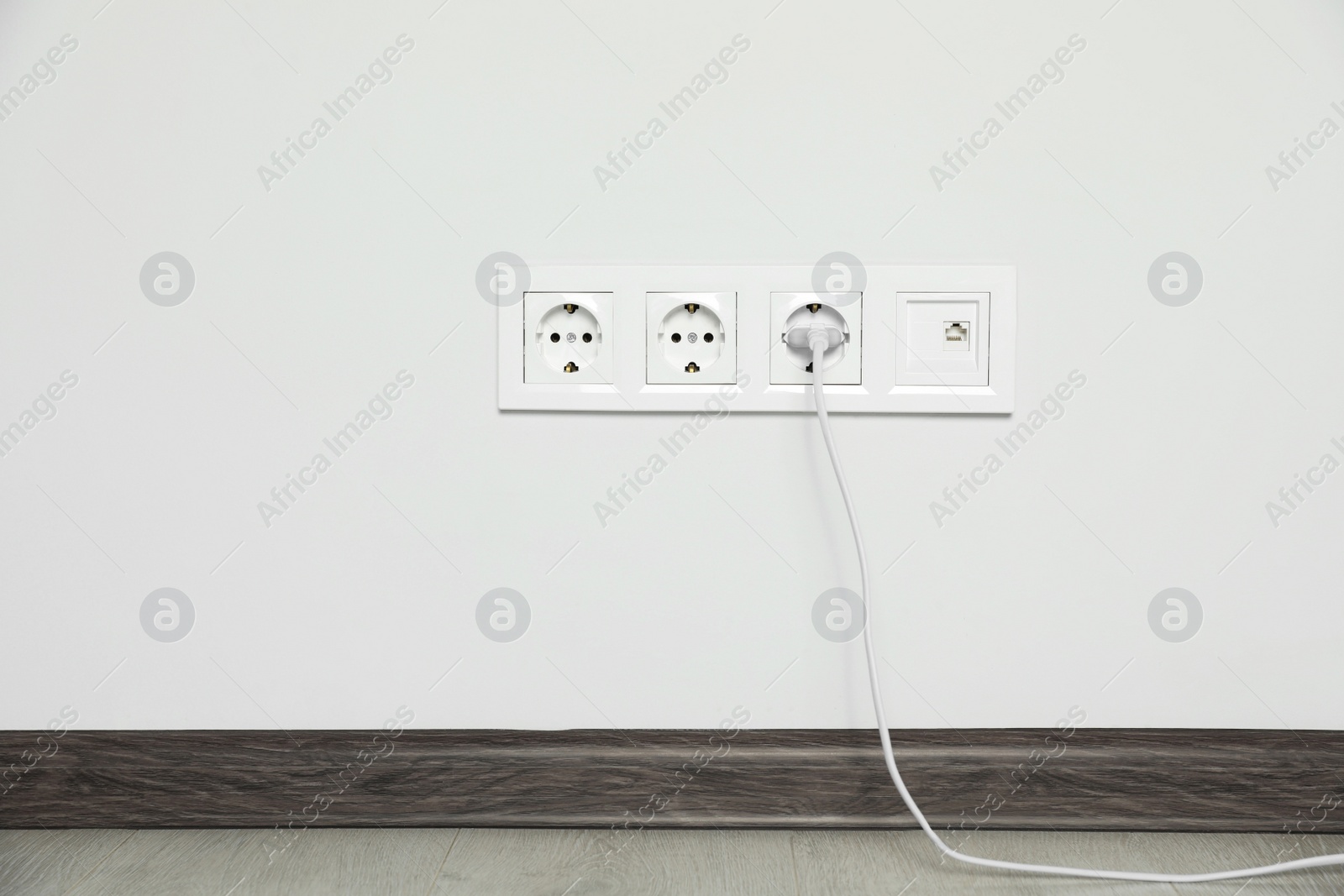 Photo of Power sockets with inserted plug on white wall indoors. Electrical supply