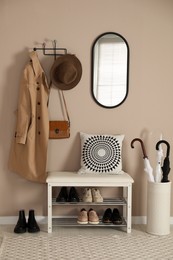 Photo of Stylish storage bench with different pairs of shoes near beige wall in hall