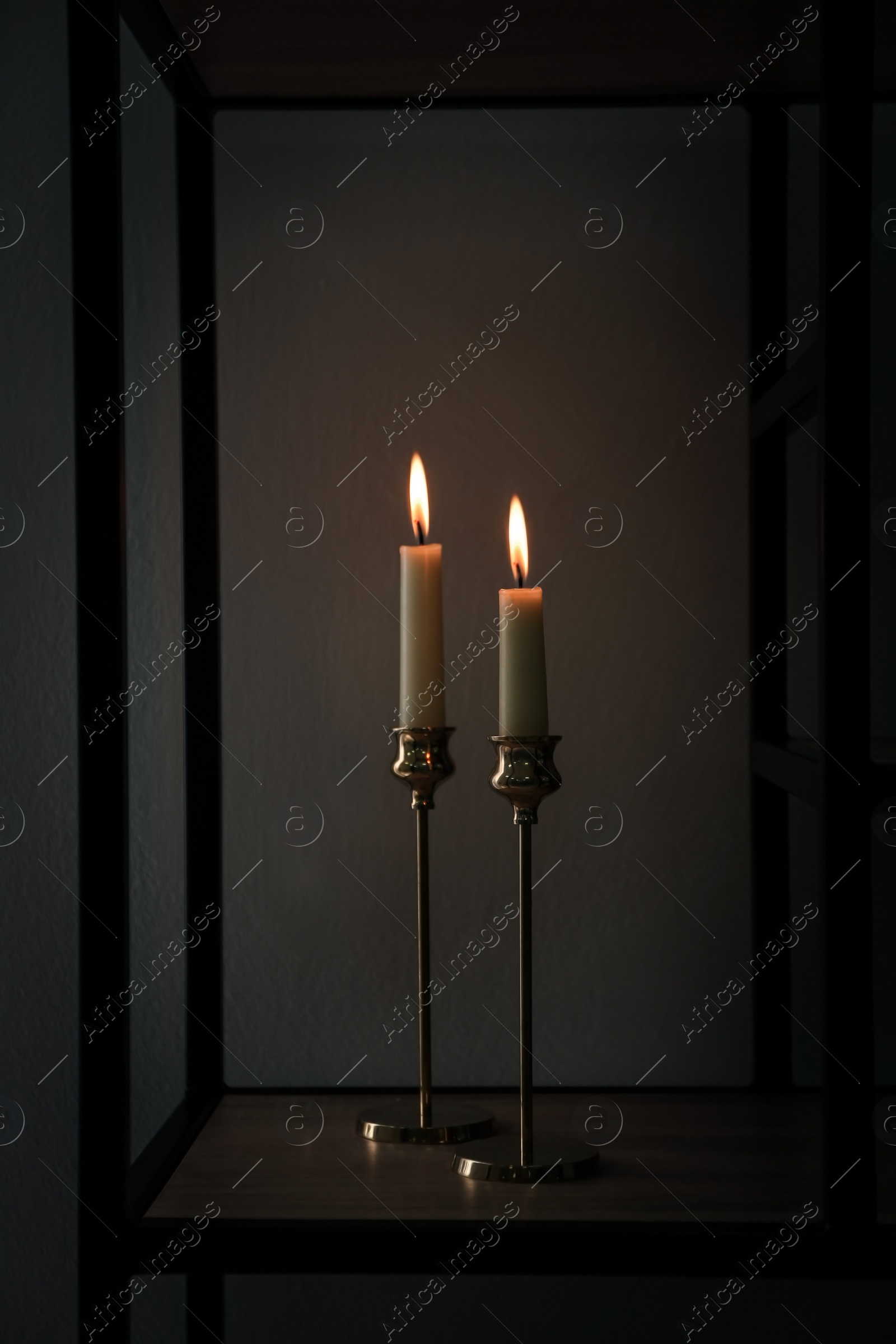 Photo of Burning candles on shelving unit in dark room