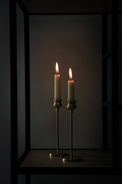 Burning candles on shelving unit in dark room