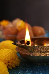 Photo of Diwali celebration. Diya lamp and chrysanthemum flowers on shiny light blue table, closeup