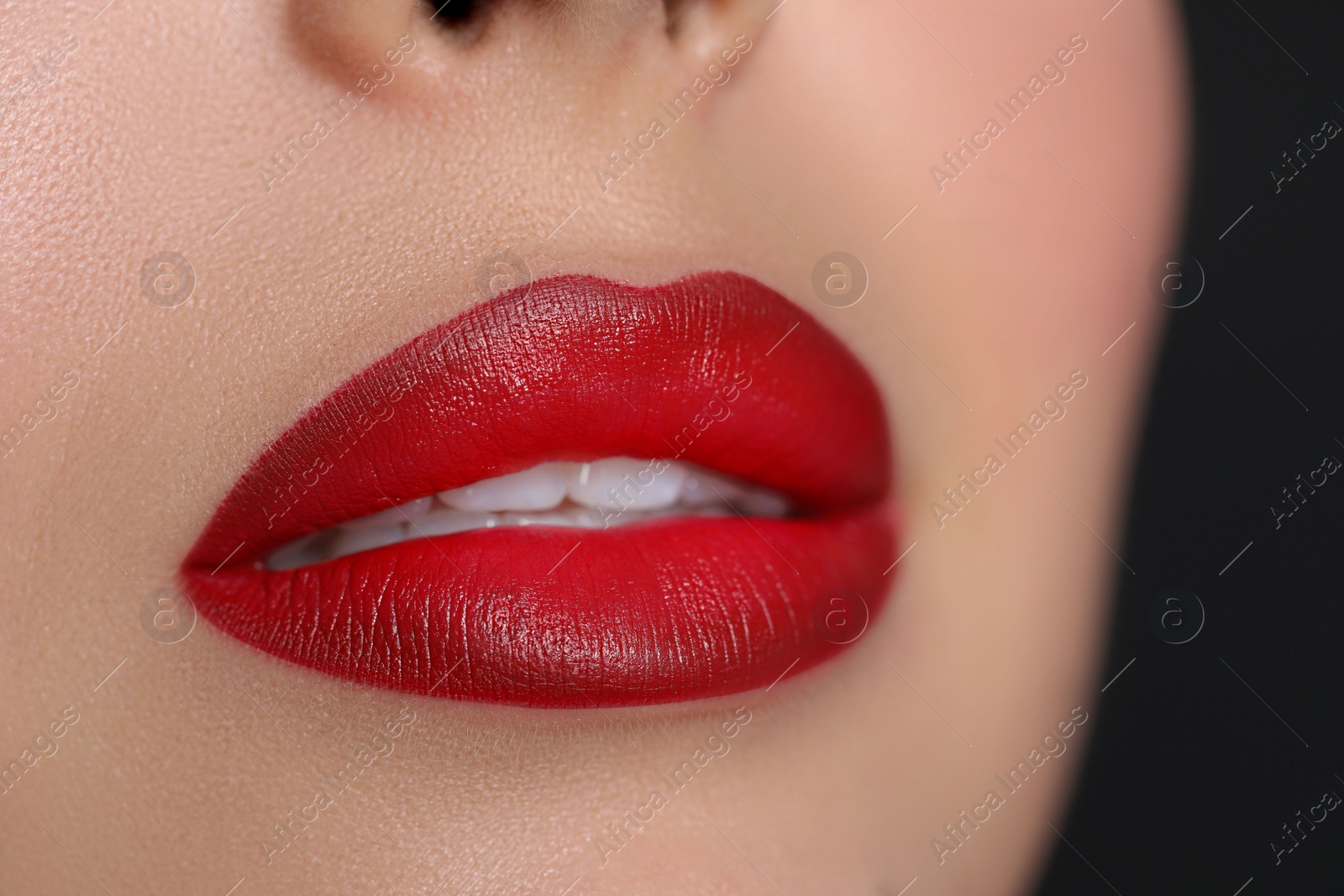 Photo of Young woman wearing beautiful red lipstick on black background, closeup