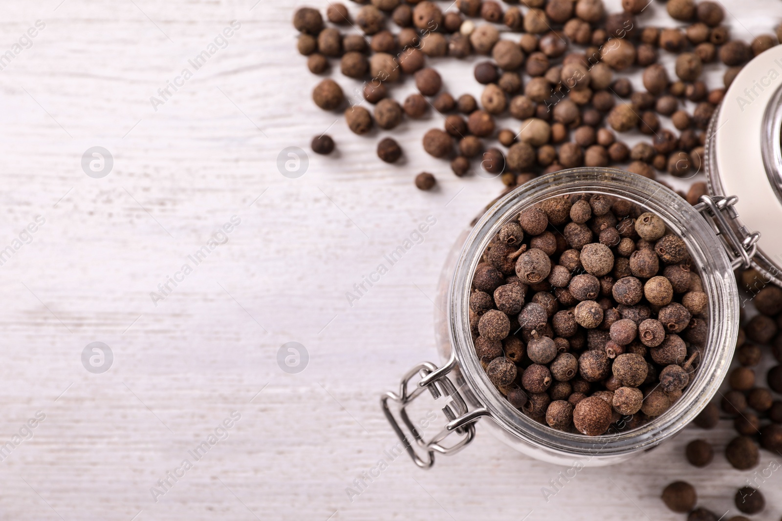 Photo of Black pepper grains on white wooden table, flat lay. Space for text