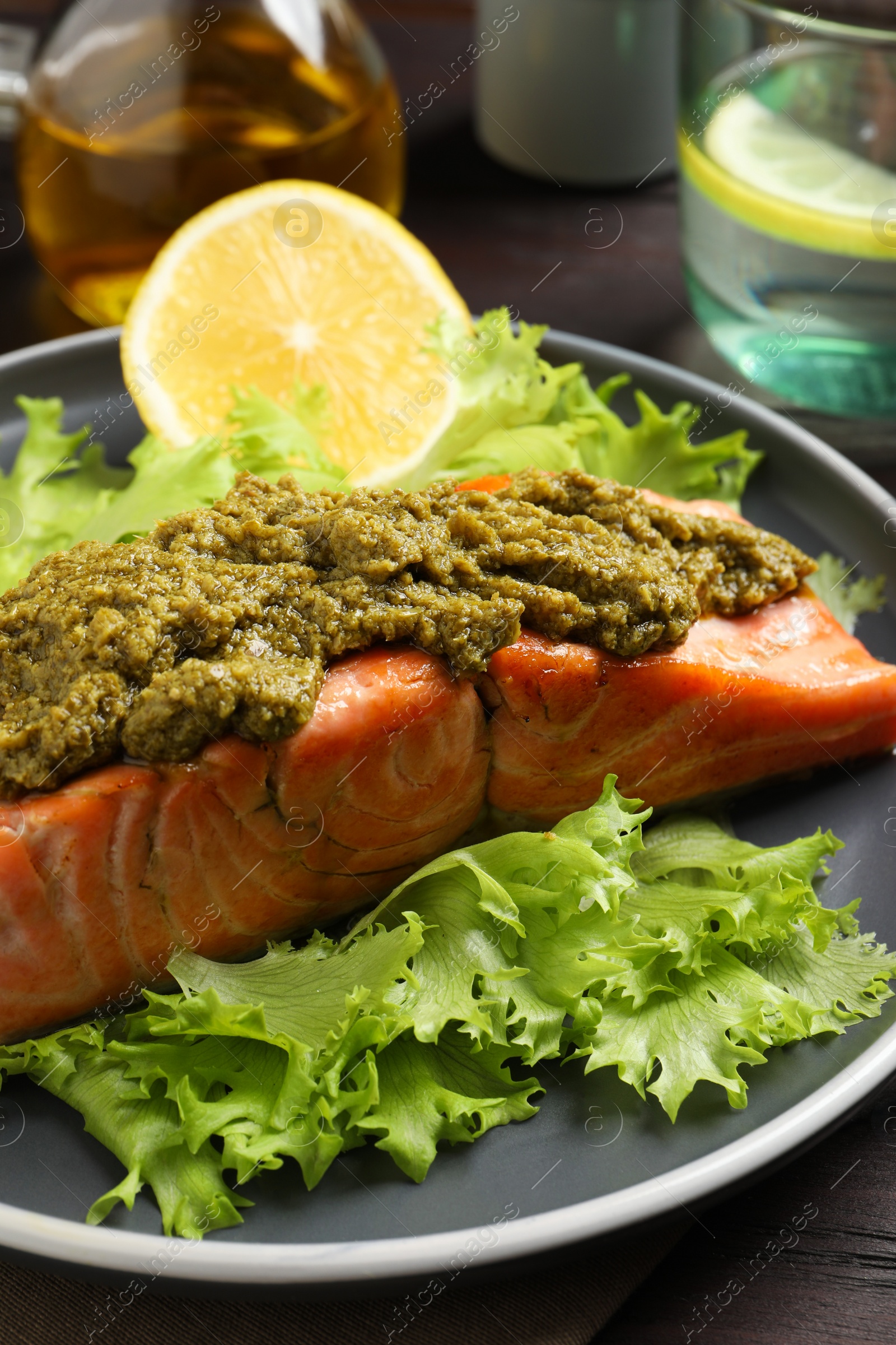 Photo of Delicious cooked salmon with pesto sauce, lettuce and lemon on wooden table, closeup