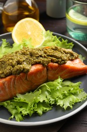 Photo of Delicious cooked salmon with pesto sauce, lettuce and lemon on wooden table, closeup