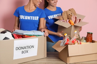 Photo of Young volunteers collecting donations at table on color background