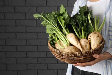 Woman holding basket with fresh sugar beets near brick wall, closeup. Space for text