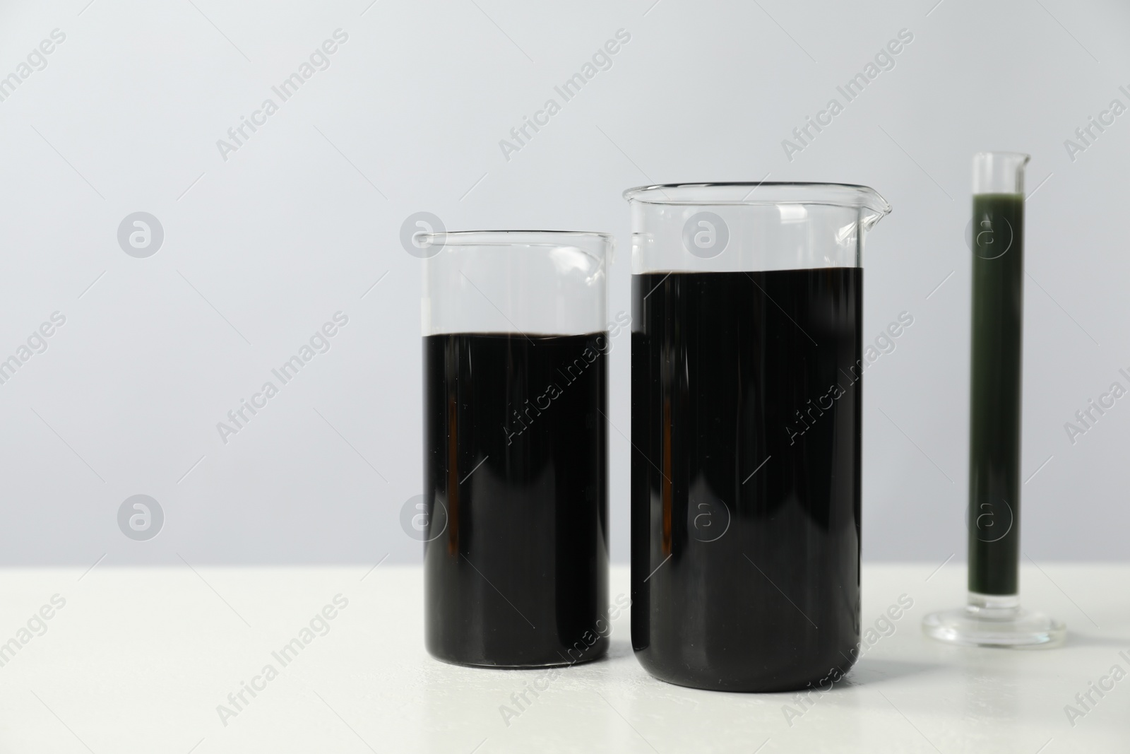 Photo of Beakers and test tube with black crude oil on white table, space for text