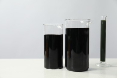 Photo of Beakers and test tube with black crude oil on white table, space for text
