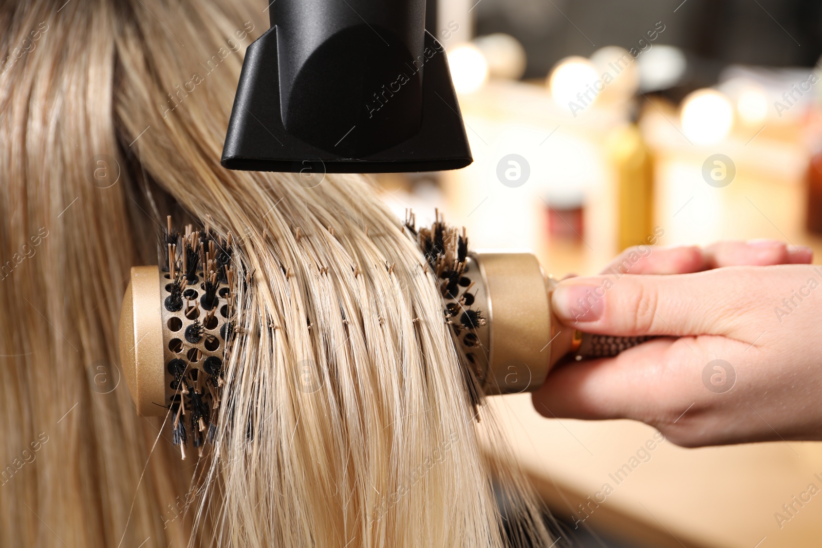 Photo of Hairdresser blow drying client's hair in salon, closeup