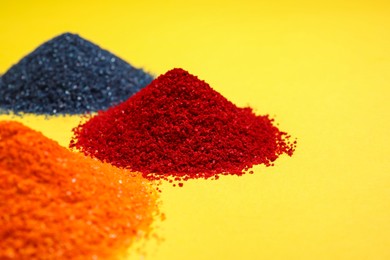 Photo of Heaps of different bright food coloring on yellow background, closeup