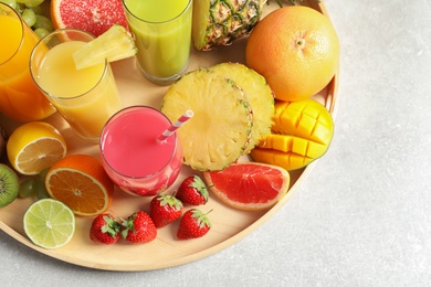 Wooden tray with glasses of different juices and fresh fruits on table, top view. Space for text