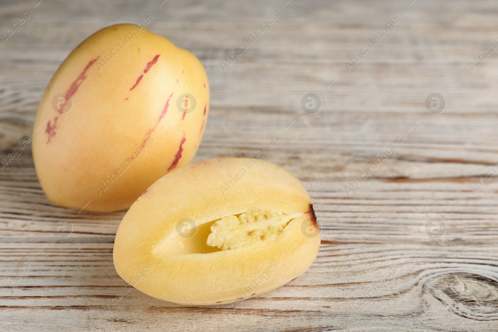 Photo of Whole and cut pepino melons on white wooden table, space for text