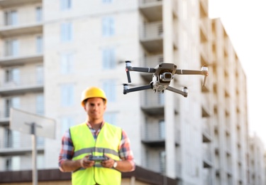 Builder operating drone with remote control at construction site, focus on quadcopter. Aerial survey