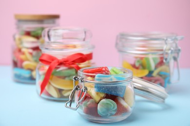 Photo of Tasty colorful jelly candies in glass jars on light blue table, closeup