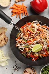 Shrimp stir fry with noodles and vegetables in wok surrounded by ingredients on grey table, flat lay