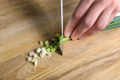 Photo of Woman cutting green spring onion on wooden board, closeup