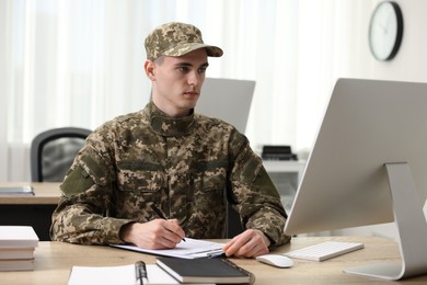 Photo of Military service. Young soldier working at wooden table in office