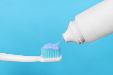 Photo of Applying paste on toothbrush against light blue background, closeup