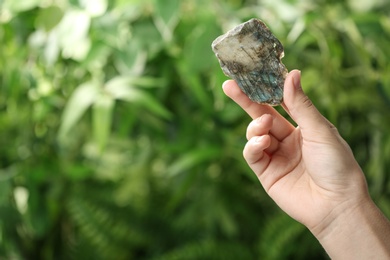 Photo of Woman holding beautiful labradorite gemstone on blurred green background, closeup. Space for text