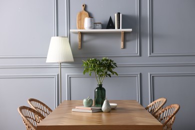 Photo of Vase with green branches, books and decor on wooden table in stylish dining room