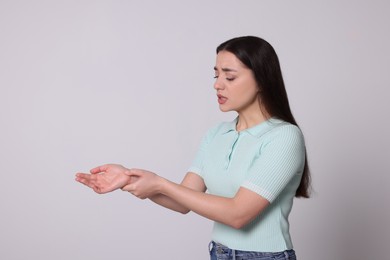 Photo of Young woman suffering from pain in hands on light grey background. Arthritis symptoms