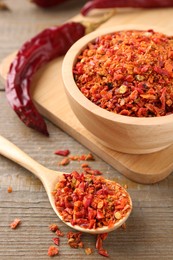 Aromatic spice. Red chili pepper flakes in bowl, spoon and pods on wooden table, closeup