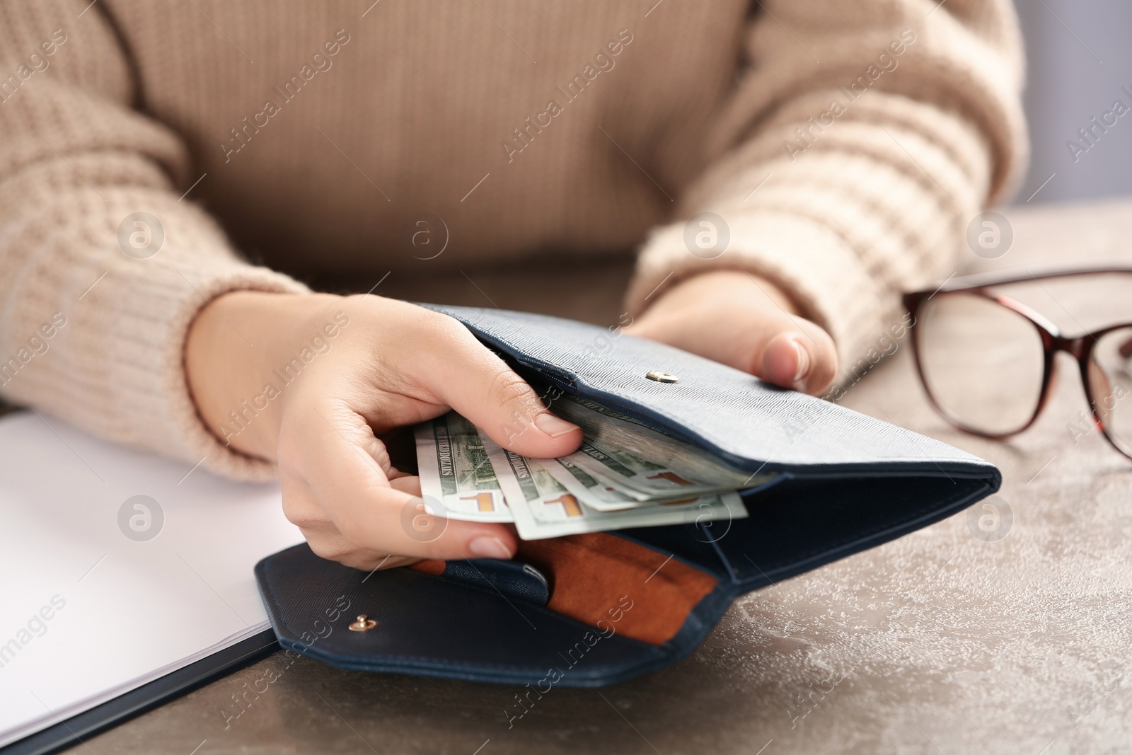 Photo of Woman putting money into wallet at brown table, closeup