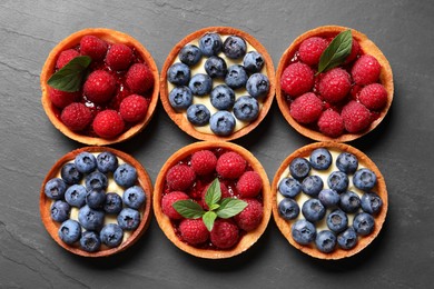 Photo of Tartlets with different fresh berries on black table, flat lay. Delicious dessert