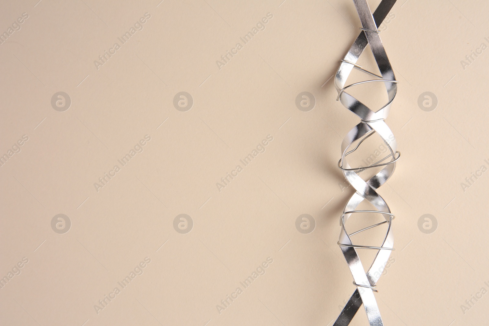 Photo of DNA molecular chain model made of metal on beige background, top view. Space for text