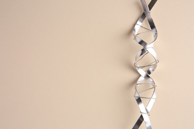 Photo of DNA molecular chain model made of metal on beige background, top view. Space for text