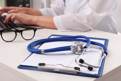 Photo of Doctor during patient consultation, clipboard and stethoscope on white table in clinic, closeup