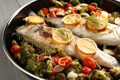 Photo of Baked fish with vegetables, rosemary and lemon on grey wooden table, closeup