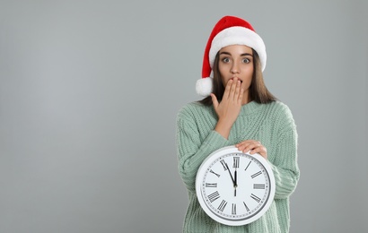 Photo of Woman in Santa hat with clock on grey background, space for text. Christmas countdown