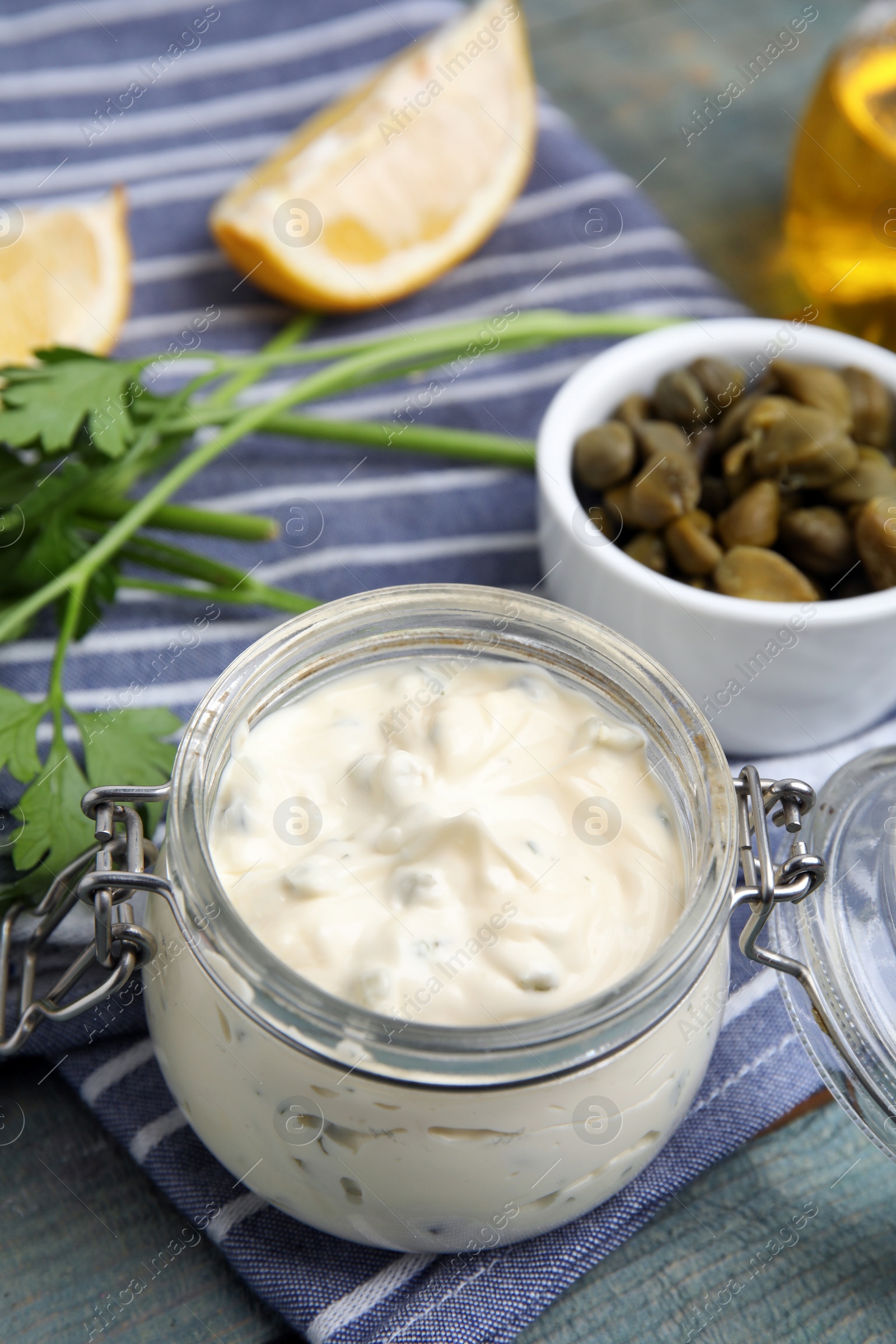 Photo of Tasty tartar sauce in glass jar and ingredients on light blue wooden table