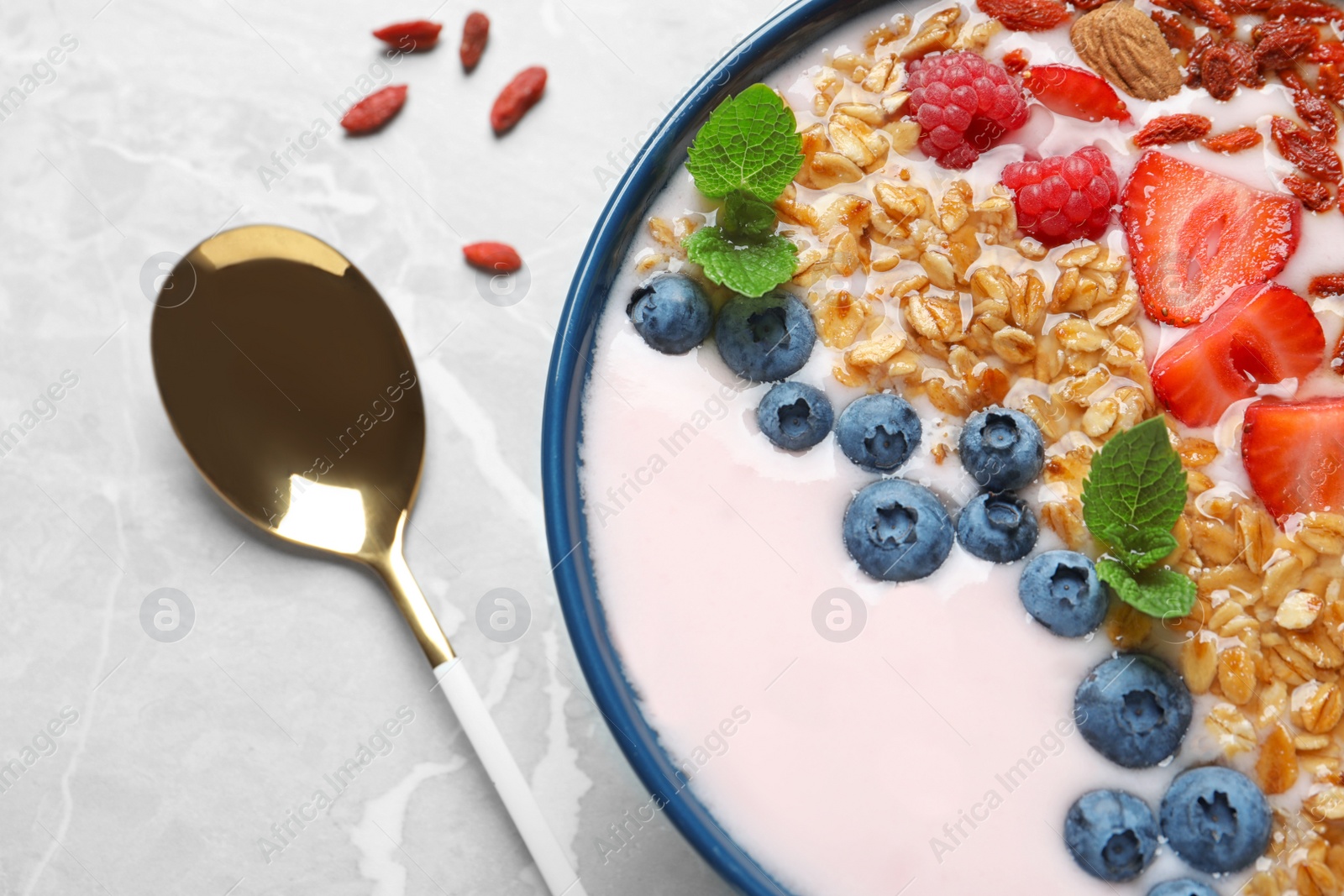 Photo of Smoothie bowl with goji berries and spoon on grey table, closeup