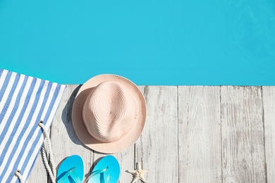 Beach accessories on wooden deck near outdoor swimming pool, flat lay. Space for text