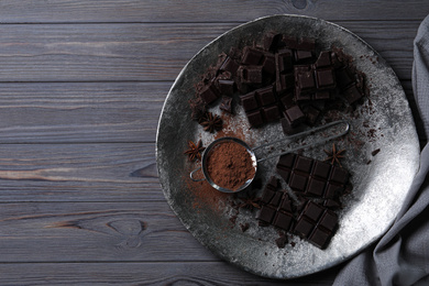 Delicious dark chocolate and cocoa powder on wooden table, flat lay