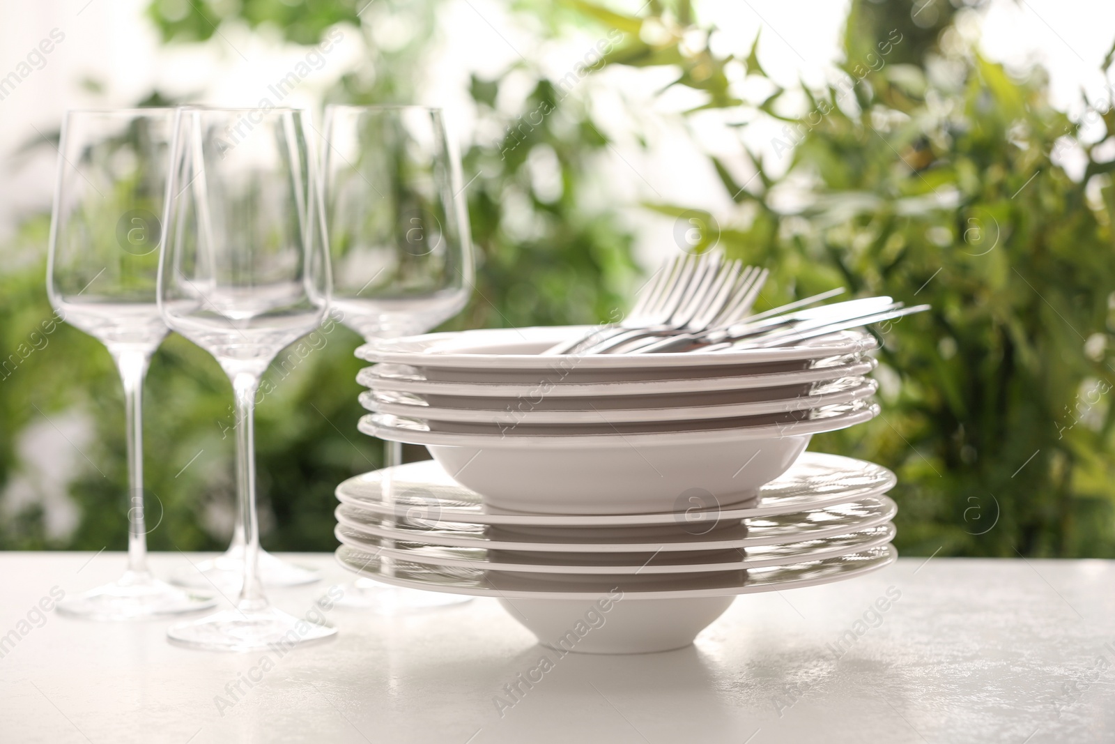 Photo of Set of clean dishware, cutlery and wineglasses on white table against blurred background