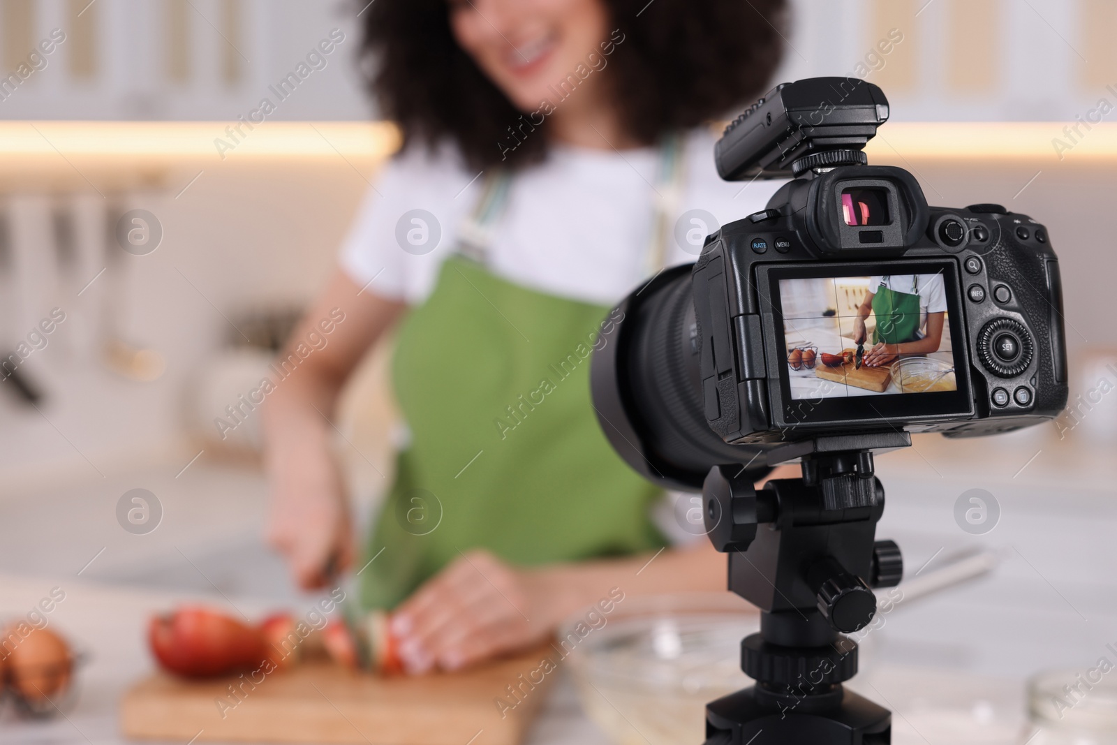 Photo of Food blogger cooking while recording video in kitchen, focus on camera