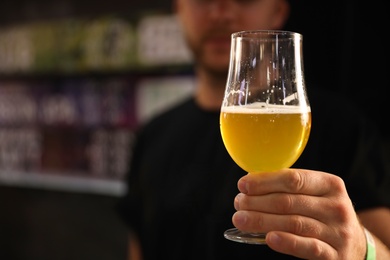 Bartender holding glass of cold tasty beer in pub, closeup