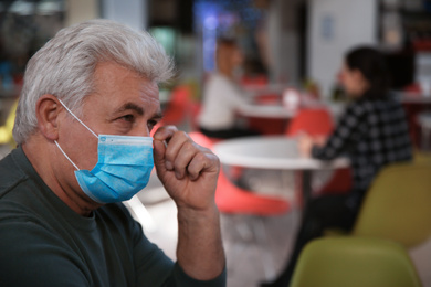 Photo of Senior man with medical mask in cafe. Virus protection