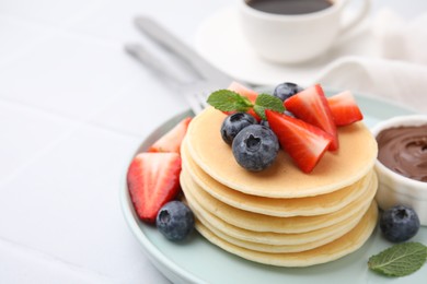 Photo of Delicious pancakes with strawberries, blueberries and mint on light table, closeup. Space for text