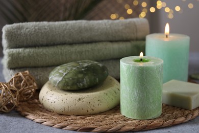 Photo of Spa composition. Burning candles, stone, soap and towels on grey table