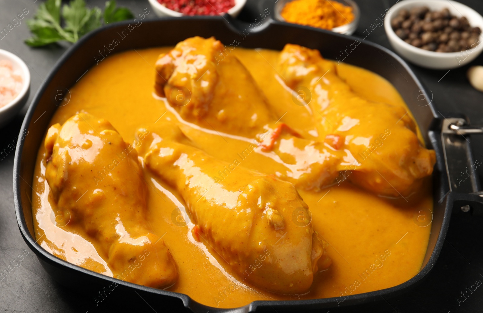 Photo of Tasty chicken curry and ingredients on black table, closeup