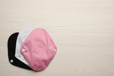 Photo of Many reusable cloth menstrual pads on white wooden table, flat lay. Space for text