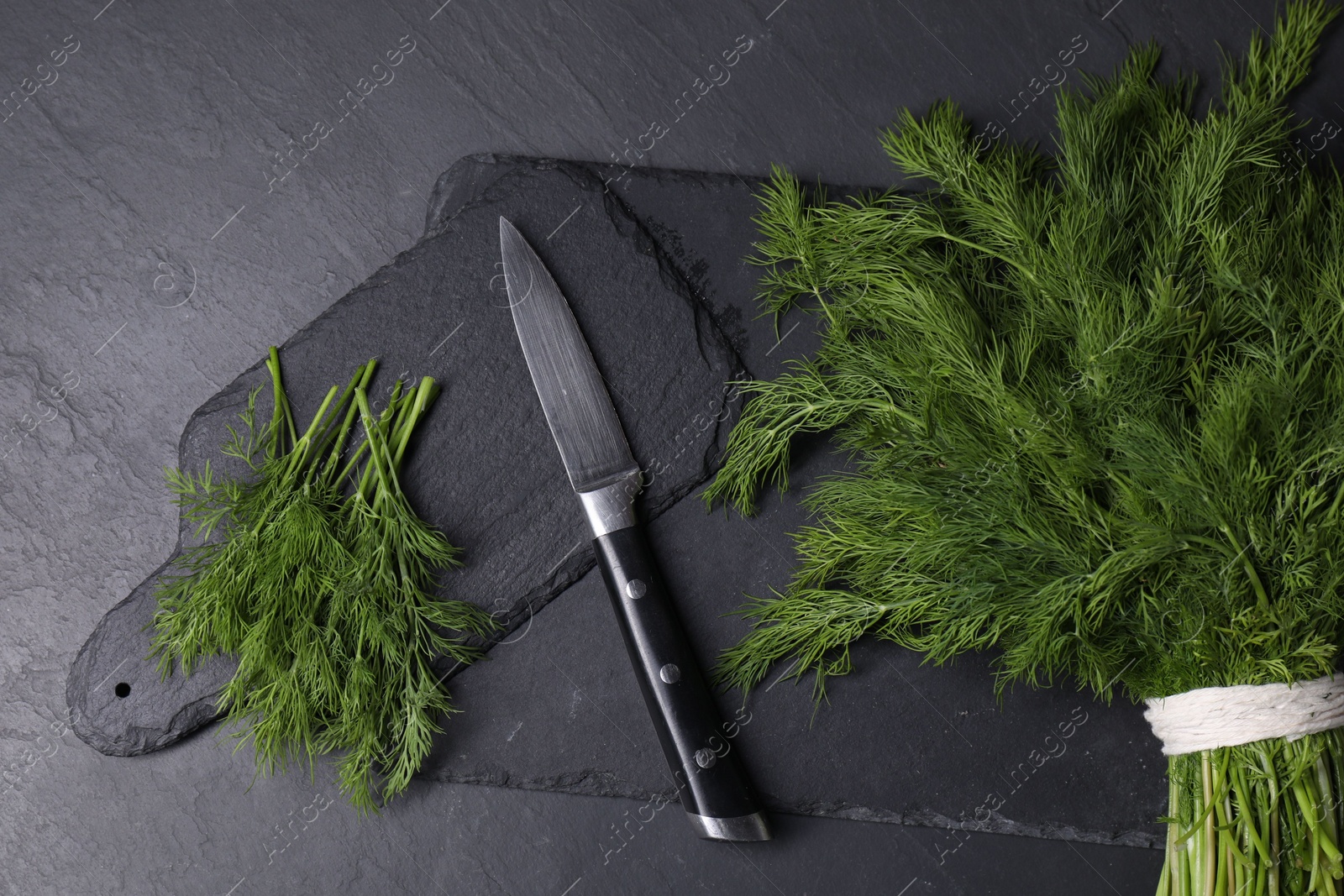 Photo of Sprigs of fresh green dill and knife on black table, top view