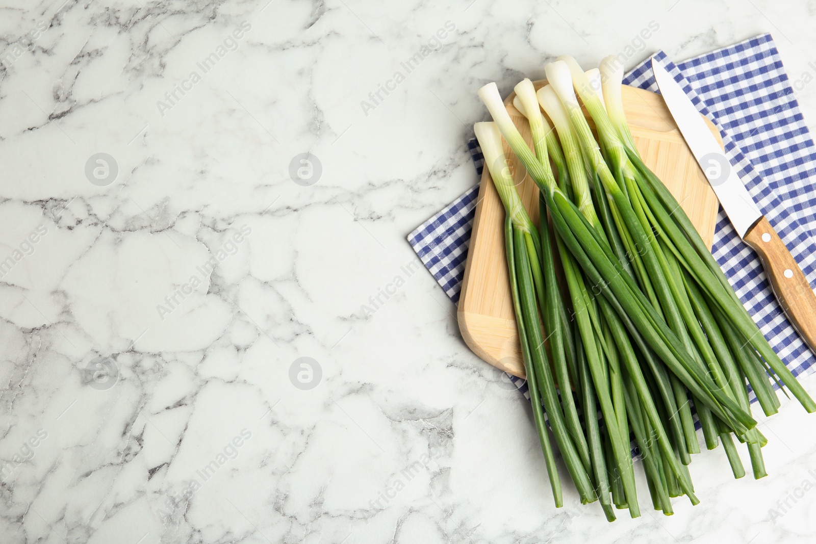 Photo of Fresh green spring onions, knife and cutting board on white marble table, flat lay. Space for text