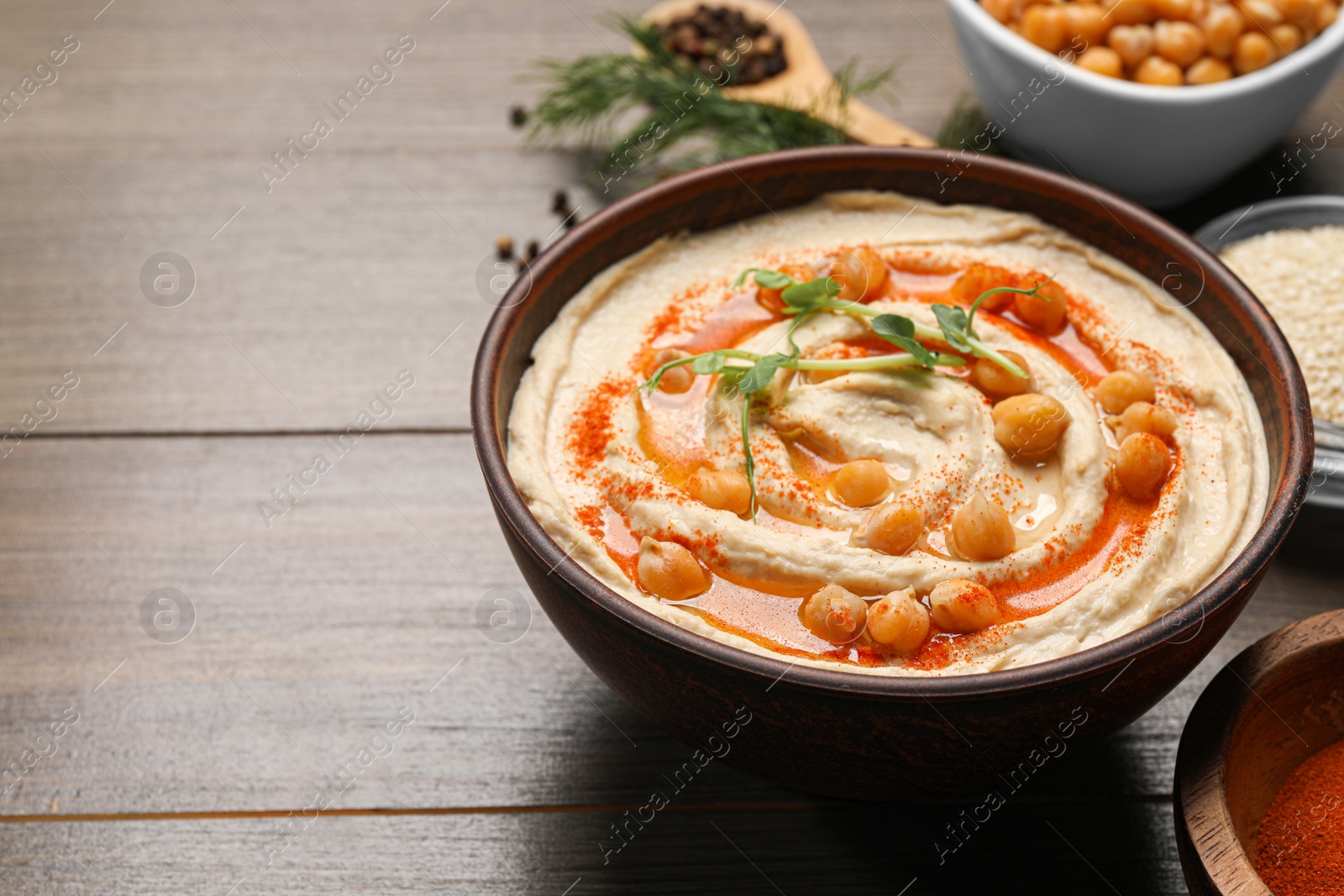 Photo of Delicious hummus with chickpeas and different ingredients on wooden table. Space for text