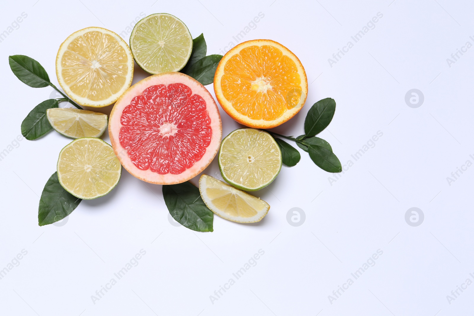 Photo of Different cut citrus fruits and leaves on white table, flat lay. Space for text